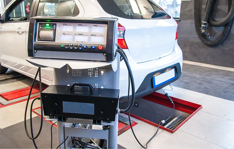 A white vehicle hooked up to an emissions reading machine.